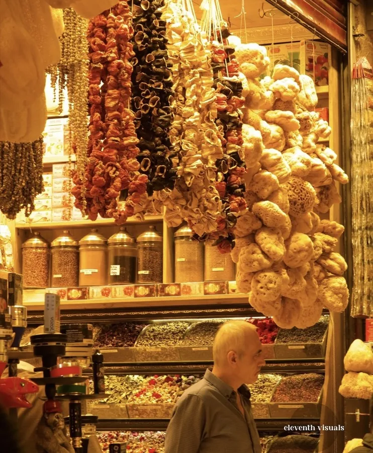 Strings of dried peppers, herbs and natural sponges hanging over spice jars at a market stall.