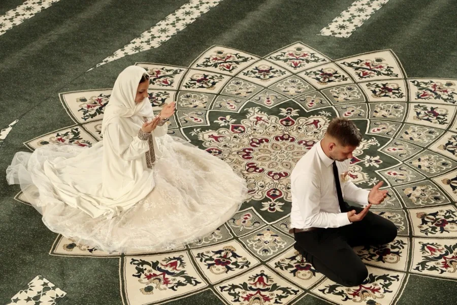 The couple kneeling in prayer on a patterned green carpet, seen from above.